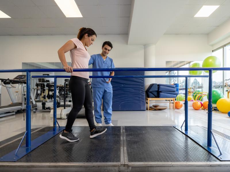 Woman doing physical therapy on bars with a doctor's assistance.